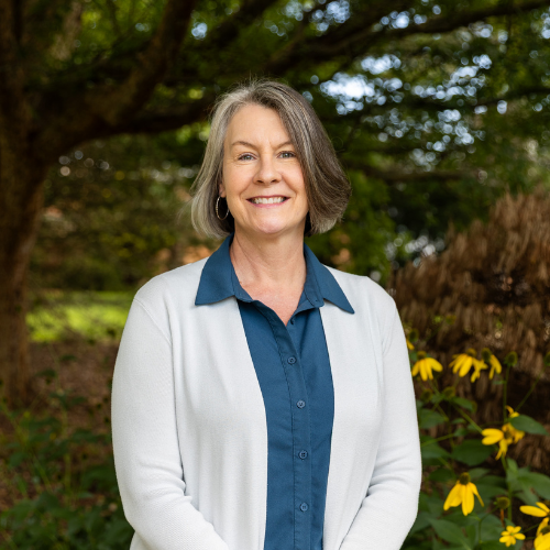 Headshot of Robin Widener, a smiling woman with shoulder-length grey-and-dark hair wearing a white cardigan over a teal collared shirt.