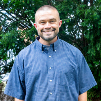 Adam Sparks, a man with short-cropped hair and a goatee, wearing a blue button-down short-sleeved shirt.