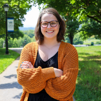 Amanda Fleenor smiling outdoors with arms crossed, wearing glasses and a rust-colored knit cardigan over a black top.