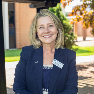 Headshot of Susan Lowe smiling, wearing a dark blue blazer with a Virginia Highlands Community College name tag, outdoors on a campus.