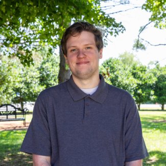 Jared Adams smiling outdoors in front of green trees, wearing a dark gray polo shirt.