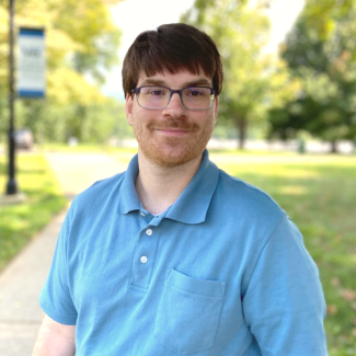 Joseph Hamil, smiling outdoors, wearing a light blue polo shirt and glasses.